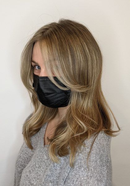Woman with brunette hair and blonde highlights and black face mask.